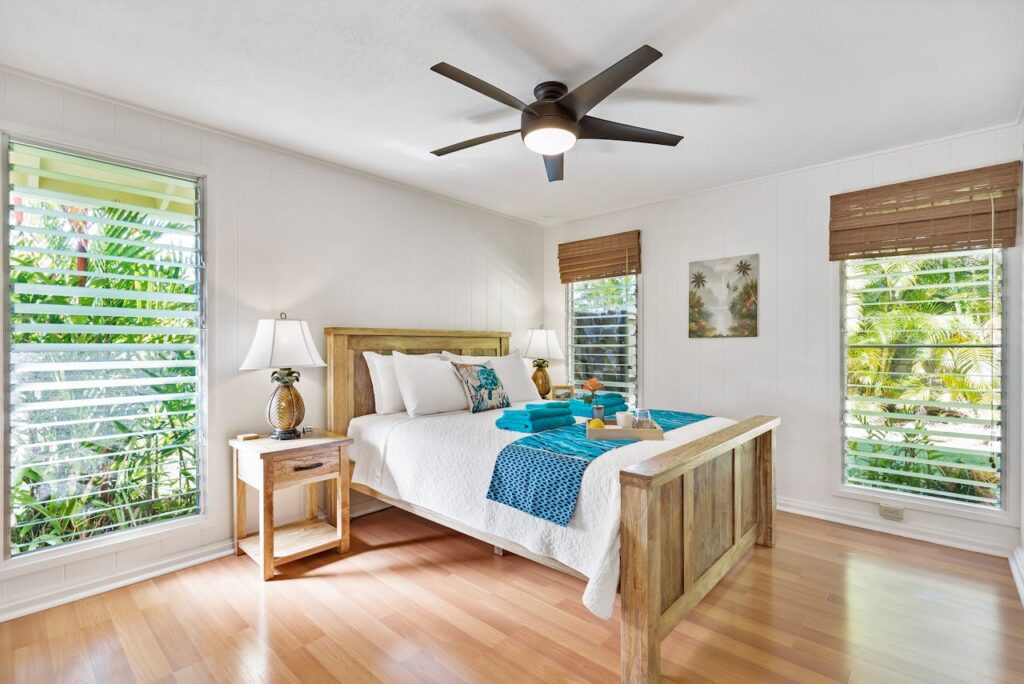 Sunny tropical bedroom with wooden furniture, teal accents, and lush greenery views.
