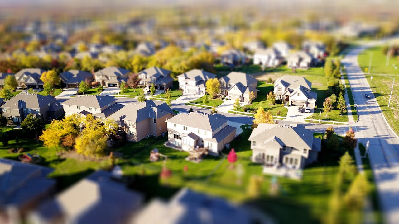 our-services-3 Tilt-shift aerial photo of a suburban neighborhood with green lawns and roads.